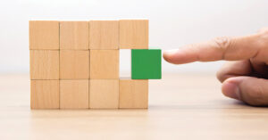 stack of wooden blocks in a 4x3 grid standing upright. There is a gap in the far-right column, middle row, where a finger is pushing in a green block to fill the gap