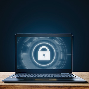 A black laptop sits on a wooden counter. The laptop screen displays a white lock symbol.