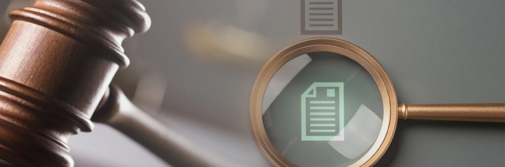 A wooden gavel next to a magnifying glass that is focused on an icon of a document