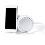 white smartphone with large black screen resting against set of white wireless over-ear headphones