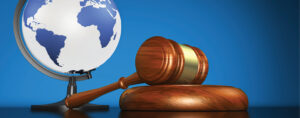 Wooden gavel resting on black on a blue background. Globe of earth resting on a stand behind and to the left