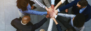 Overhead photo of several individuals bringing hands together in the middle of a standing huddle