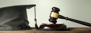 Wooden gavel resting on a block; gray mortarboard cap with tassel at left