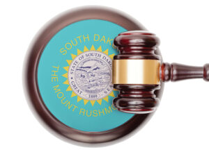 Wooden gavel and block; block has a light blue background ringed with wood with the great seal of the State of South Dakota in its center