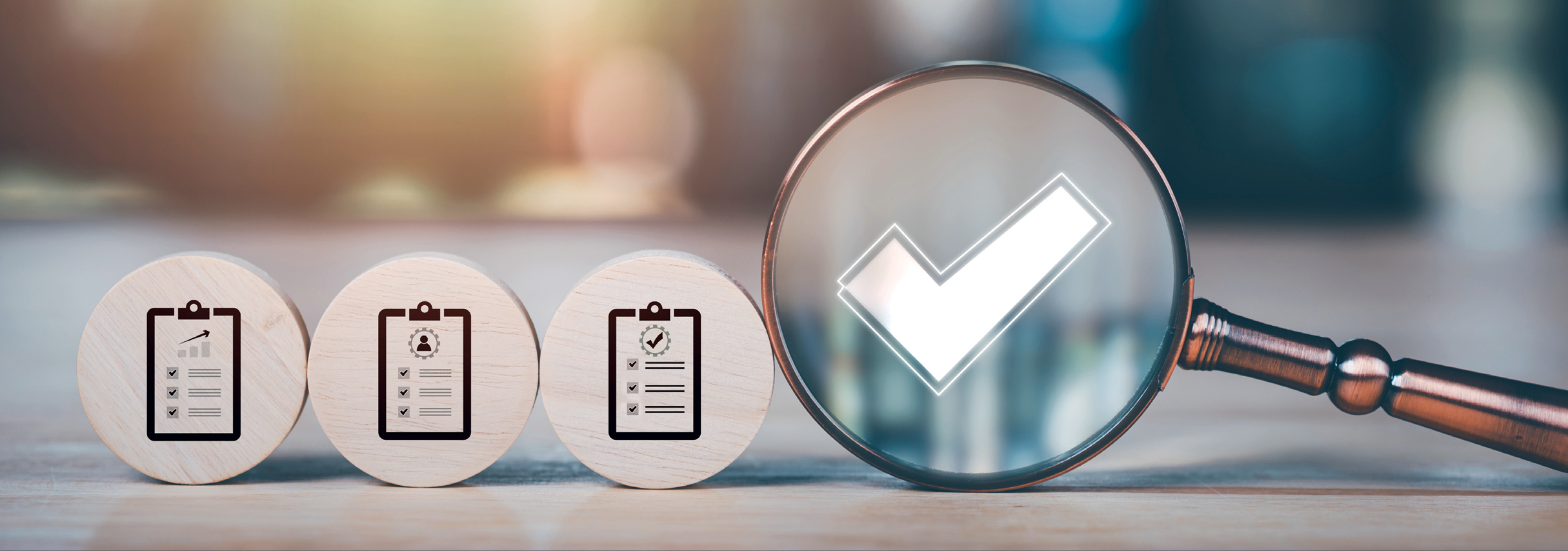 3 wooden discs standing up on their edges with icons of simplified documents on them, leaning against a larger magnifying glass with a large white check mark in the lens