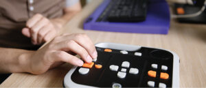 Closeup of person using adaptive controller at desk next to a computer keyboard
